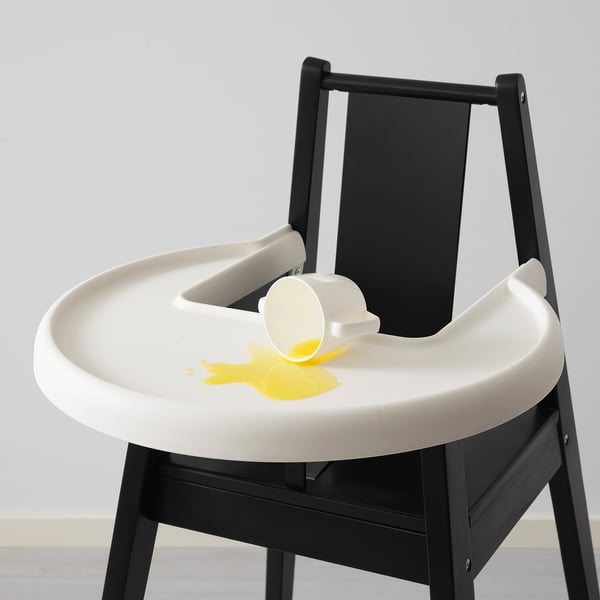 Highchair with removable tray, designed for young children. White tray, black frame. Spilled yellow liquid on tray. Safe and sturdy for feeding.