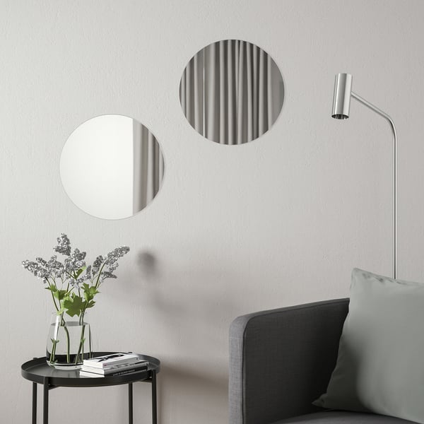 Round mirrors above side table with flowers, books; grey chair, wall light.