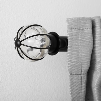 Glass and metal curtain finial mounted on wall, holding light grey curtain.