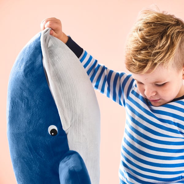 A child wearing striped pyjamas is hugging a plush blue whale soft toy.