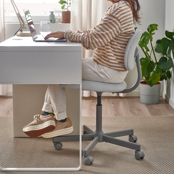 A person sits at a BLECKBERGET office chair, feet on desk, working on a laptop; the chair has a backrest, armrests, and swivel castors.