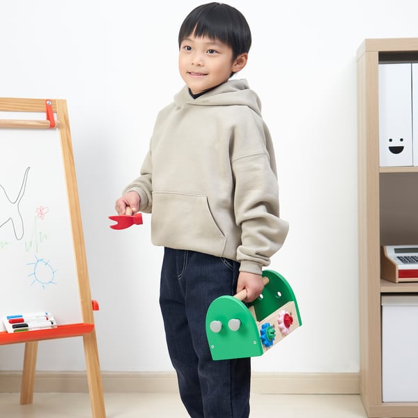 Young boy holding a red toy plane and a green toy toolbox with colourful accessories, aimed at developing motor skills and creativity.