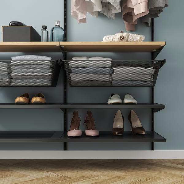 Modern closet with shelves holding folded clothes in mesh baskets and pairs of shoes neatly arranged on dark shelves. Clothes hang above on hangers.