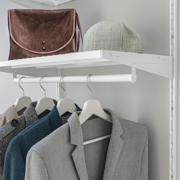 White closet shelf holding brown bag and green cap, below hangers with grey coats.
