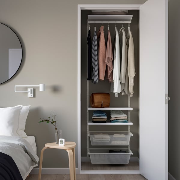 Neatly organised closet with hanging tops, folded clothes, baskets, and a side table with plant.