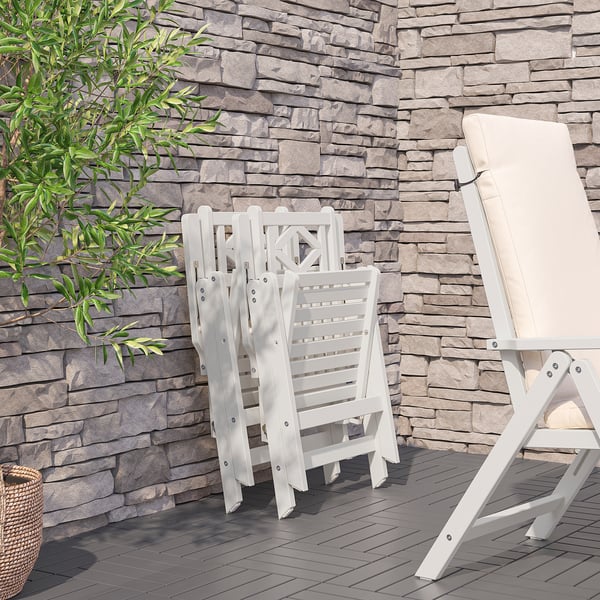 Outdoor patio with white acacia reclining chairs from bondholmén, foldable, against stone wall.