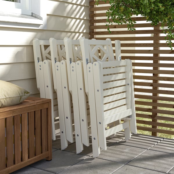 Folded white chairs stored on patio; wooden bench and fence nearby.