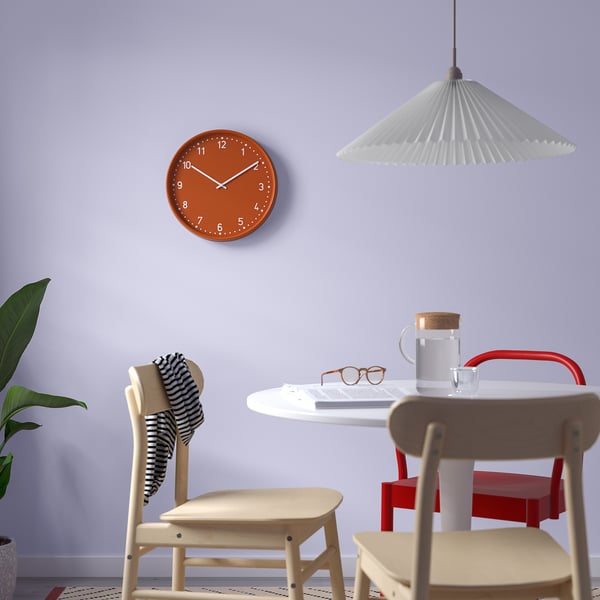 Modern room with orange BONDIS clock, wooden chairs, white table, lamp, and plants.