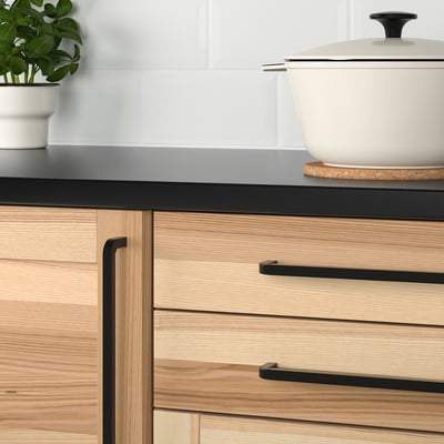 Modern kitchen drawers with light wood and black handles.