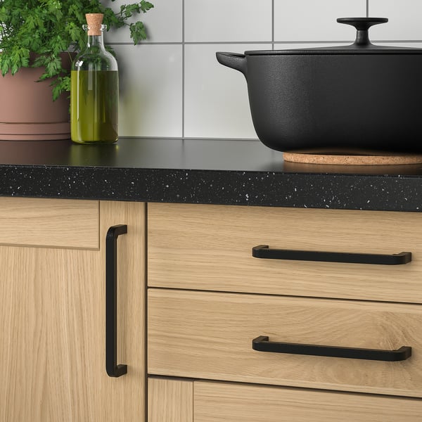 Cast iron pan on counter, beside wooden cabinets and green plant.