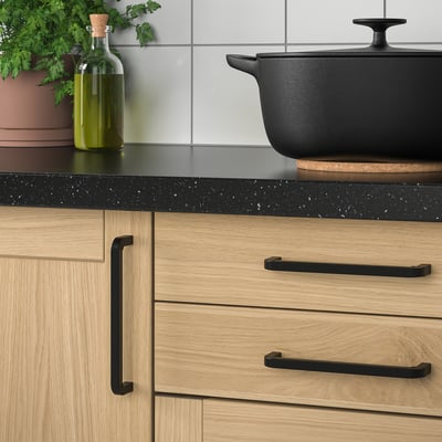 Cast iron pan on counter, beside wooden cabinets and green plant.