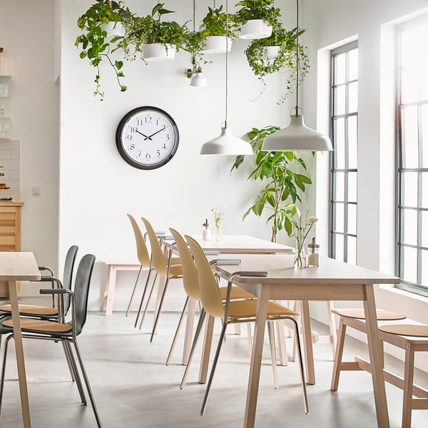 Spacious, modern kitchen with white dining set, plants, and a silent, black-framed round clock on the wall.