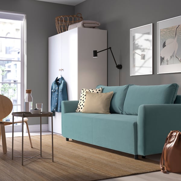 Modern living room with teal BRISSUND sofa, white cabinet, and wall art. Sofa is large, fitting multiple cushions.