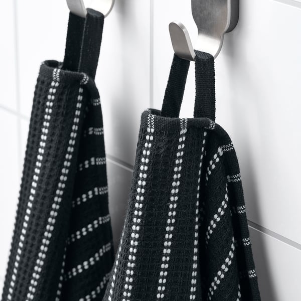 Black towels with white patterns hang on metal hooks. The towels feature a waffle texture for absorbency and terry surface for softness.