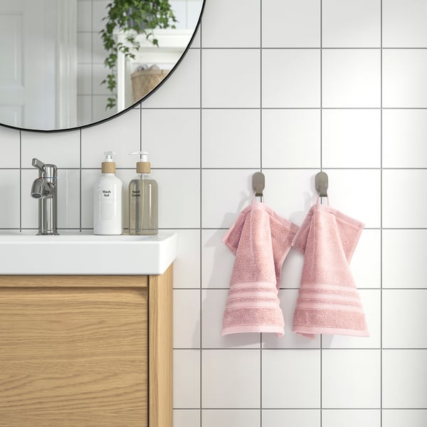 Pink towels hang on hooks near sink with soap dispensers, reflective mirror above.