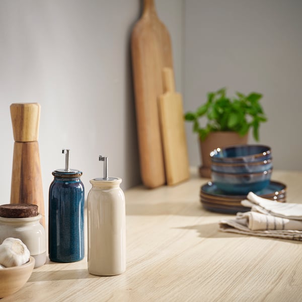 BRUGDHAJ rustic stoneware dispenser. White, with stainless pour spout. Smaller than adjacent wooden bottle.