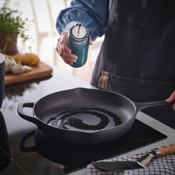 A person seasoning a skillet with a blue oil bottle.