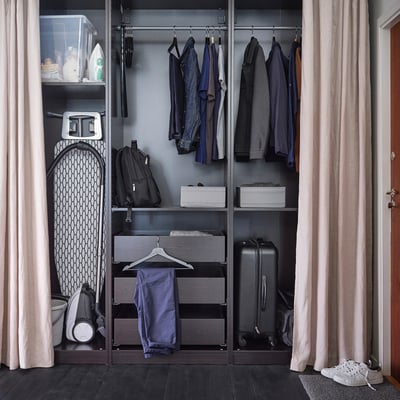 Closed closet with ironing board, clothes, and luggage. BUMERANG hangers visible; white iron, dark board.