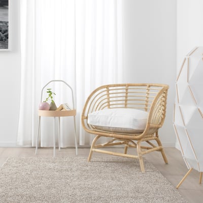 The BUSKBO chair is a hand-woven light beige rattan armchair with a natural, airy, and sturdy design, featuring protective plastic feet.