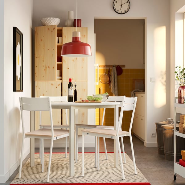 Modern white BUSLÄTT chair set around a small dining table with wooden cabinet in background.