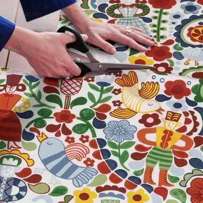 Person cuts colourful, patterned fabric with scissors. The fabric folk art designs, suitable for sewing projects.