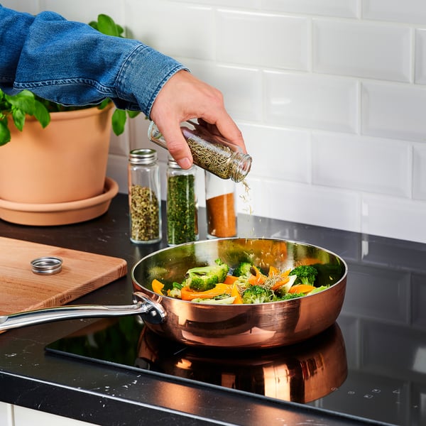 Person adds spice from CITRONHAJ jar to pan with colourful vegetables on stove.
