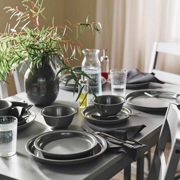 Dining table with grey DAGGASTER dinnerware, vase with green branches, and neatly arranged cutlery and napkins.