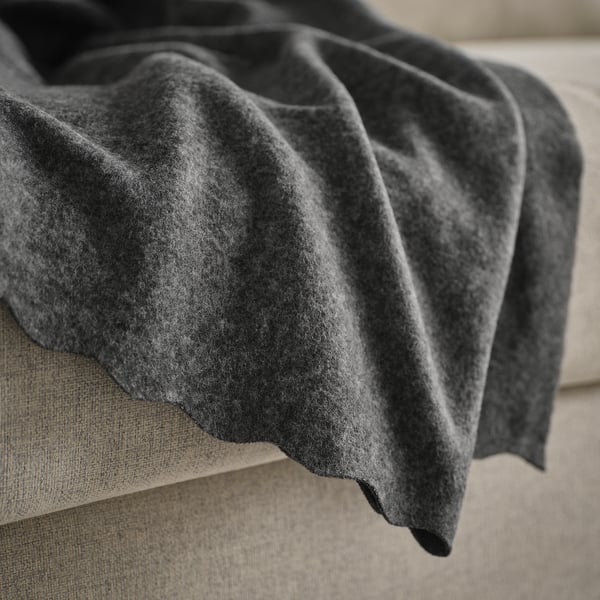 A soft, dark grey fleece blanket draped over a beige couch or bed. The texture looks cosy and inviting, ideal for warmth.