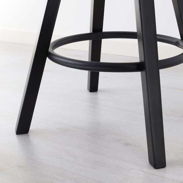 Black metal stool with circular footrest and adjustable height, on light wooden floor. High quality materials ensure stability and durability.