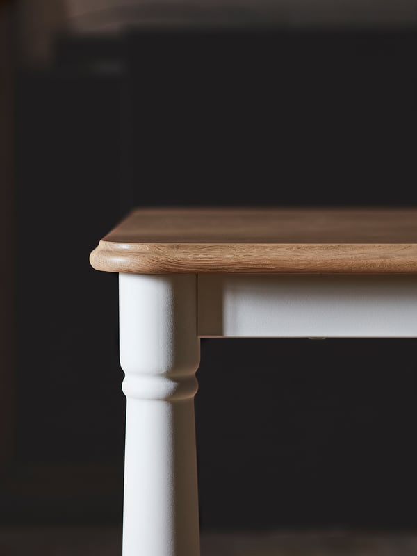 Wooden table against dark background. White painted legs, oval top. Modern minimalist design.