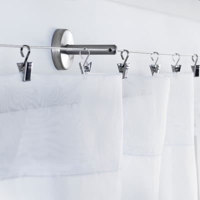 Stainless steel curtain rod with adjustable angle fittings, supporting white curtains.