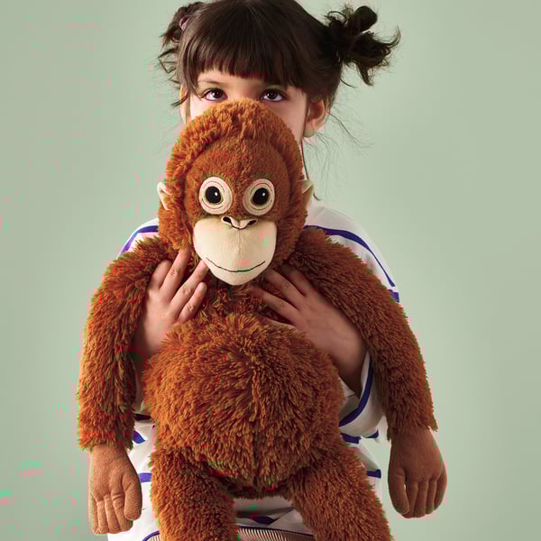 A young girl holds a plush, huggable orangutan soft toy designed to hang around the person body, showcasing its secure, touch-and-close fasteners.