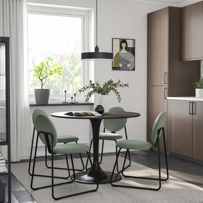 Modern dining setup with a black DOCKSTA table and mint-green chairs. Light, airy room with a large window, stylish decor, and wooden cabinet.