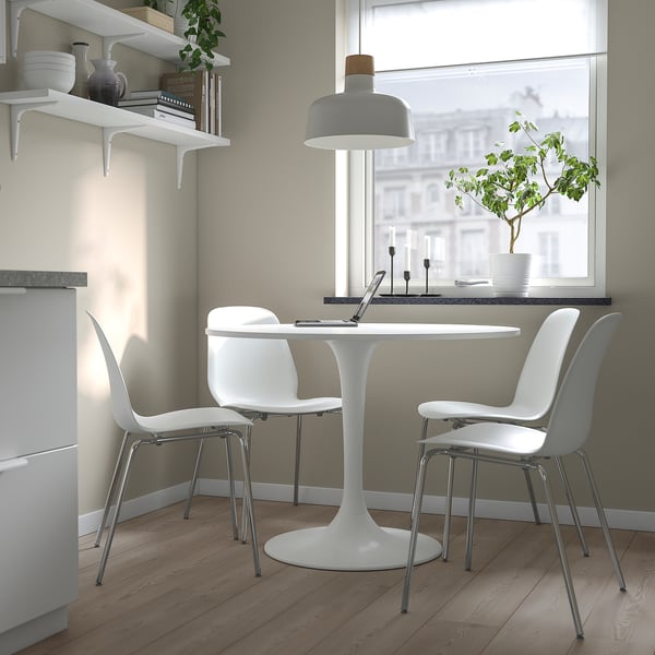 Small white DOCKSTA dining table with round shape, surrounded by white chairs, positioned near a window with a view.