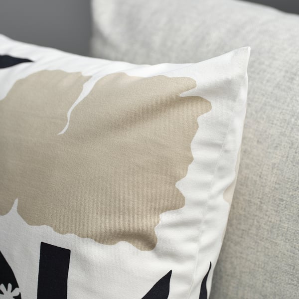 A close-up of a soft, white cotton cushion cover with a subtle, textured pattern of stylized flowers, laying on a light-colored surface.