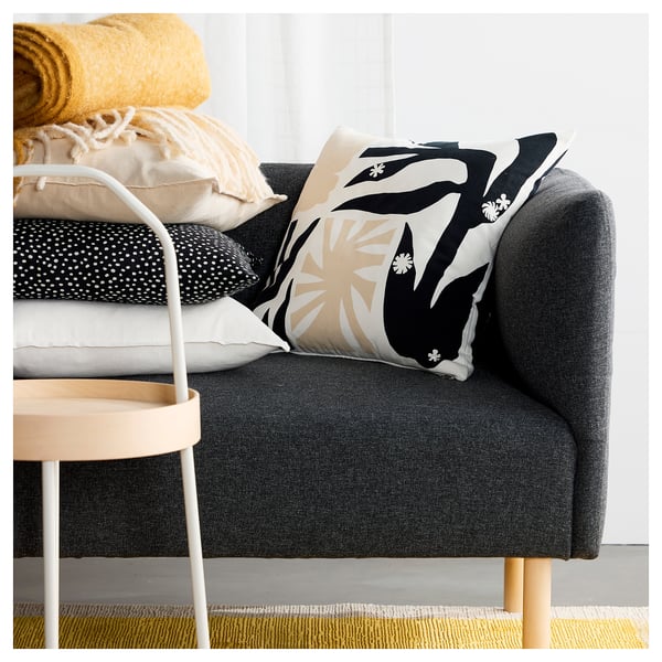 Image dark grey DRABOR cushion with black & beige floral pattern on a sofa, surrounded by other cushions and a yellow throw.