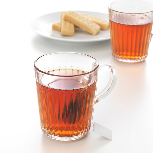 Two glass mugs with tea and a tea bag string hanging out, accompanied by a plate with three cookies.