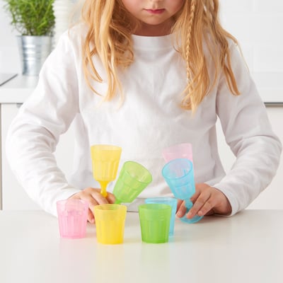 Girl plays with colourful cups & glasses, stacking, imagining.