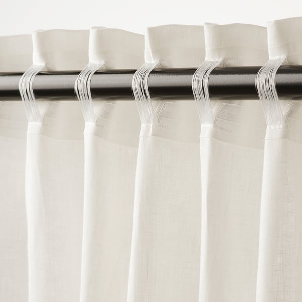 White curtains hang with pleats, allowing light through while providing privacy. Metal rod and hooks visible at the top.