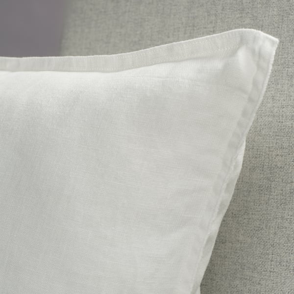 Close-up of a white linen cushion cover on a grey surface, showcasing its soft, textured material and clean stitching.