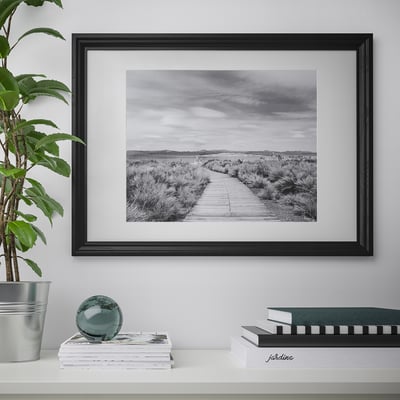 Black frame on wall with black & white path to horizon, desk with magazines, plant, glass sphere.