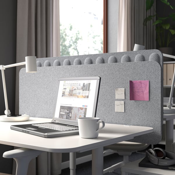 Grey polyester felt office screen with rounded top, behind desk with laptop, cup, and lamp, offering privacy.