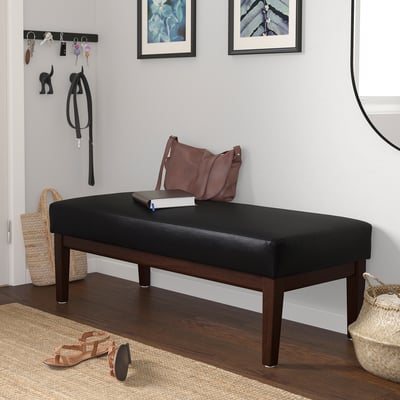 Black bench with brown handles against wall, near coat & sandals.