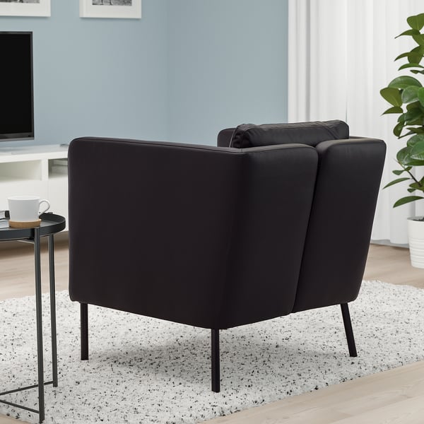 Modern dark armchair with moveable back cushion, on sleek metal legs, in cosy room setting.