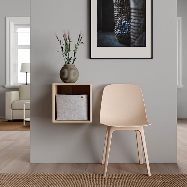 Light-wood chair next to wall-mounted cabinet with grey box, decorative plant.
