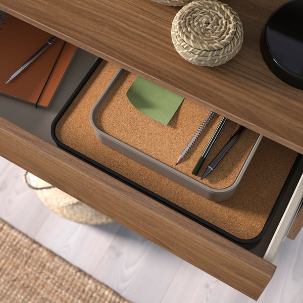 Desk with open drawer holding pens, paper, and a notepad.