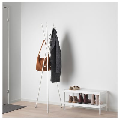 White EKRAR coat stand with hooks holds a brown bag and grey sweater; next to it, a white shoe rack with boots.