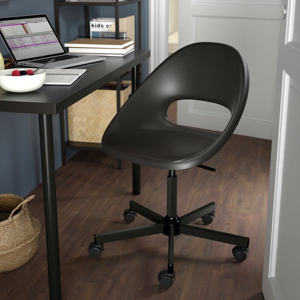 Black ELDBERGET adjustable office chair with casters beside a dark desk with a laptop and fruit bowl.
