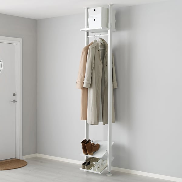 A white ELVARLI storage system with shelves and a clothes rail. Its tall, holding coats and boots, placed beside a white door.