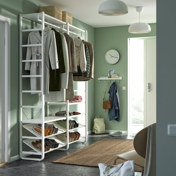 Organised green entryway with white ELVARLI storage system, shelves, and hanging coats. Rug and wall hooks visible.